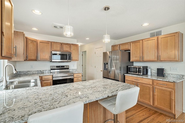 kitchen with visible vents, light wood finished floors, a peninsula, a sink, and appliances with stainless steel finishes