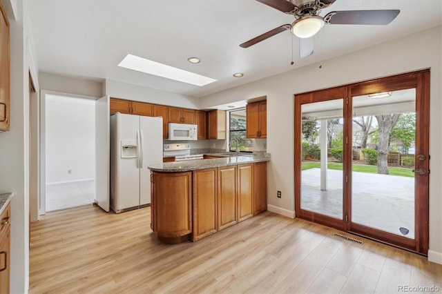 kitchen with white appliances, light wood finished floors, visible vents, brown cabinets, and a skylight
