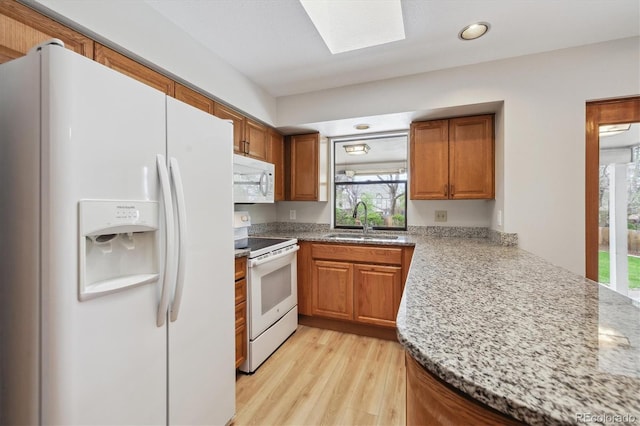kitchen with a sink, brown cabinetry, white appliances, and plenty of natural light