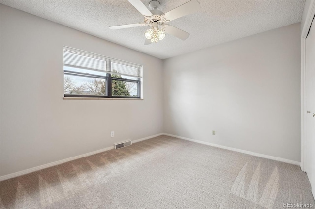 spare room with light colored carpet, a textured ceiling, a ceiling fan, and visible vents
