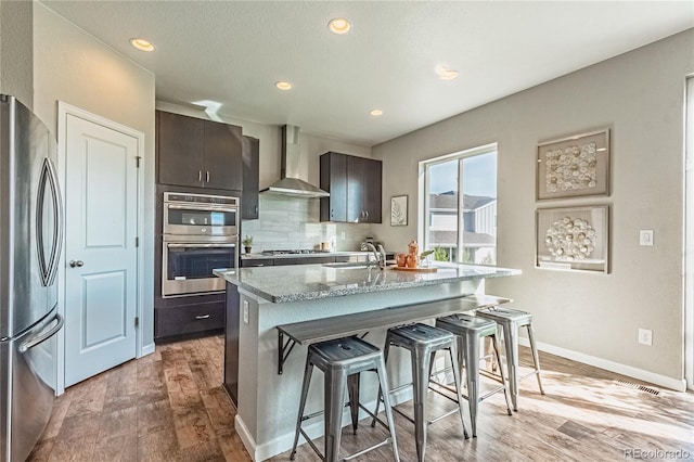 638 W 175th Ave, Broomfield, CO 80023 - kitchen featuring wall chimney range hood, appliances with stainless steel finishes, a breakfast bar area, light wood-type flooring, and tasteful backsplash