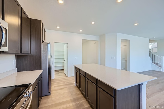 kitchen featuring a kitchen island, stainless steel appliances, light stone counters, light hardwood / wood-style flooring, and dark brown cabinets