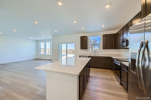 kitchen with light hardwood / wood-style flooring, appliances with stainless steel finishes, sink, light stone countertops, and a center island