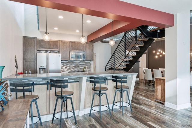 kitchen featuring refrigerator with ice dispenser, a kitchen bar, pendant lighting, and decorative backsplash