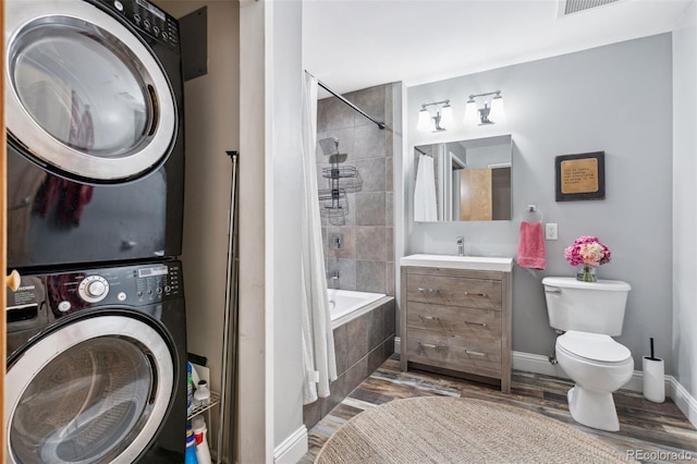 full bathroom featuring toilet, stacked washer / dryer, tiled shower / bath, vanity, and hardwood / wood-style floors