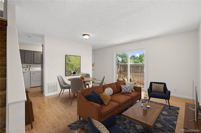 living room featuring light wood-type flooring, separate washer and dryer, and a textured ceiling