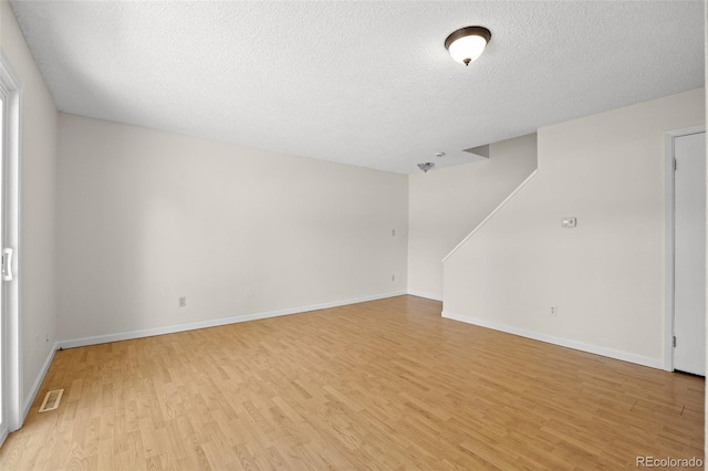 empty room with a textured ceiling and light hardwood / wood-style flooring