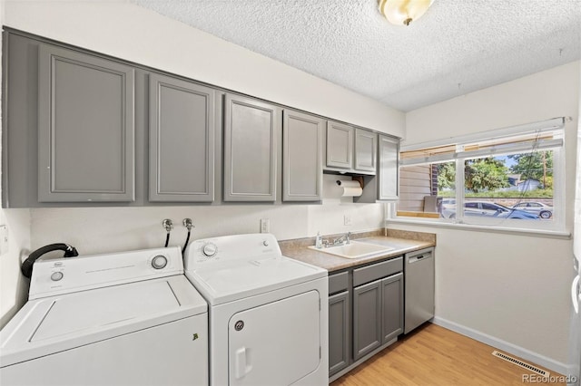 laundry area featuring cabinets, a textured ceiling, sink, light hardwood / wood-style flooring, and independent washer and dryer