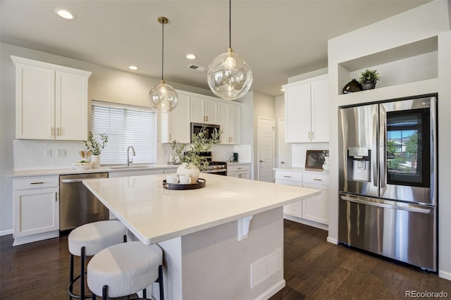6689 Backcountry Loop, Colorado Springs, CO 80927 - kitchen featuring appliances with stainless steel finishes, dark wood-style flooring, backsplash, white cabinetry, and a kitchen bar