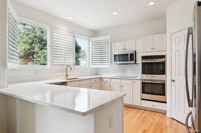 kitchen with kitchen peninsula, appliances with stainless steel finishes, white cabinets, and sink