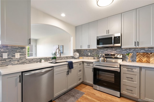 kitchen with light hardwood / wood-style floors, tasteful backsplash, sink, gray cabinetry, and stainless steel appliances