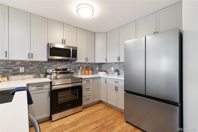 kitchen with appliances with stainless steel finishes, white cabinetry, tasteful backsplash, and light hardwood / wood-style flooring