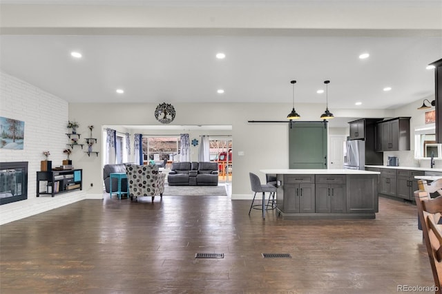 kitchen with pendant lighting, light countertops, open floor plan, a kitchen island, and stainless steel fridge