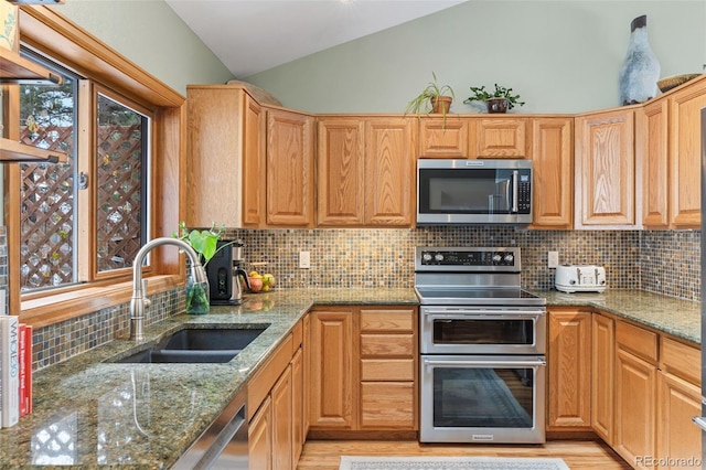 kitchen featuring sink, tasteful backsplash, vaulted ceiling, appliances with stainless steel finishes, and light stone countertops