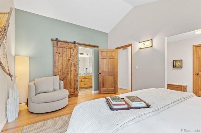 bedroom with ensuite bathroom, a barn door, wood-type flooring, and lofted ceiling