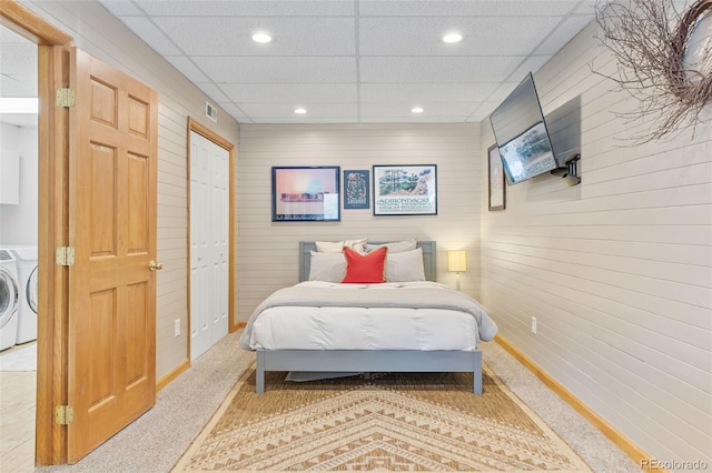 bedroom with a paneled ceiling, wooden walls, a closet, light colored carpet, and washer and clothes dryer