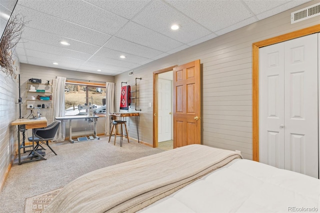 carpeted bedroom featuring a paneled ceiling, a closet, and wood walls