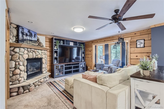 living room featuring carpet, ceiling fan, a stone fireplace, and wooden walls