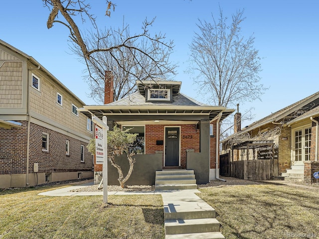 view of front of property with entry steps, fence, a front yard, brick siding, and a chimney