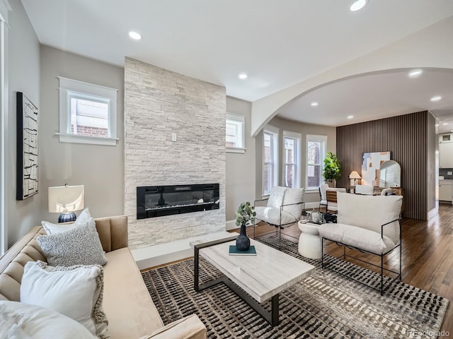 living room with baseboards, a stone fireplace, recessed lighting, wood finished floors, and arched walkways