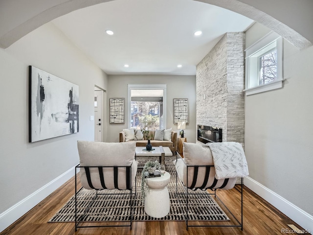 sitting room featuring arched walkways, a fireplace, baseboards, and wood finished floors