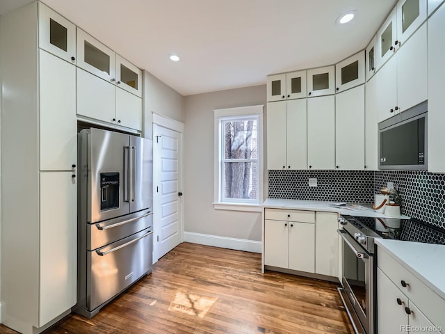 kitchen with decorative backsplash, light countertops, high end appliances, and wood finished floors