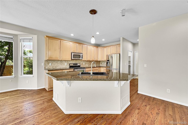 16500 Hitching Post Cir, Parker, CO 80134 - kitchen with appliances with stainless steel finishes, light brown cabinetry, a kitchen bar, wood finished floors, and tasteful backsplash