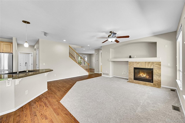 16500 Hitching Post Cir, Parker, CO 80134 - unfurnished living room with a ceiling fan, a tiled fireplace, wood finished floors, stairs, and recessed lighting