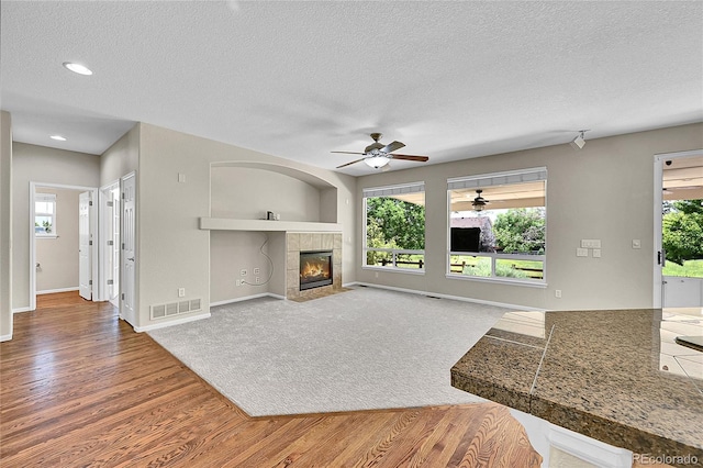 16500 Hitching Post Cir, Parker, CO 80134 - unfurnished living room with wood finished floors, a ceiling fan, a textured ceiling, a tiled fireplace, and healthy amount of natural light