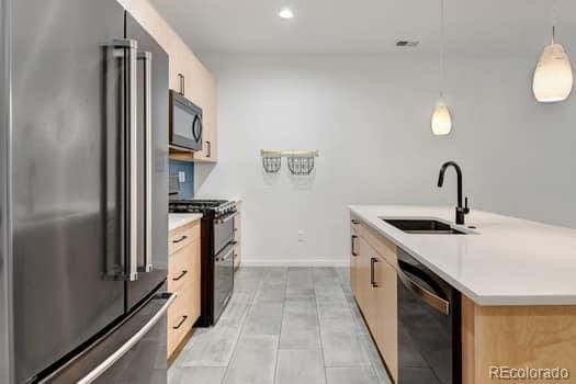 kitchen with sink, stainless steel appliances, decorative light fixtures, light brown cabinets, and a kitchen island with sink