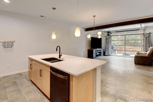 kitchen featuring black dishwasher, light brown cabinetry, sink, decorative light fixtures, and a center island with sink