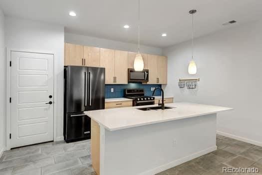 kitchen with light brown cabinets, a kitchen island with sink, black appliances, pendant lighting, and sink