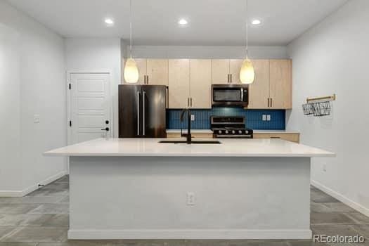 kitchen featuring light brown cabinets, hanging light fixtures, a kitchen island with sink, sink, and stainless steel appliances