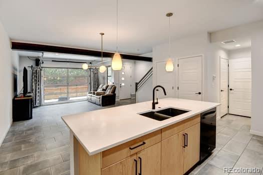 kitchen featuring black dishwasher, light brown cabinetry, sink, pendant lighting, and a kitchen island with sink