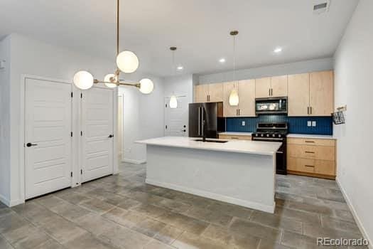 kitchen featuring decorative backsplash, a center island with sink, decorative light fixtures, light brown cabinetry, and appliances with stainless steel finishes