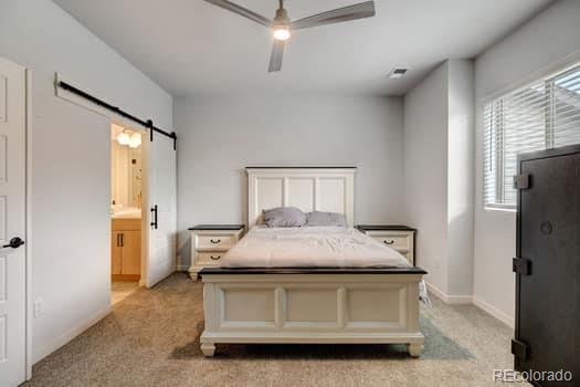 bedroom featuring a barn door, light colored carpet, connected bathroom, and ceiling fan