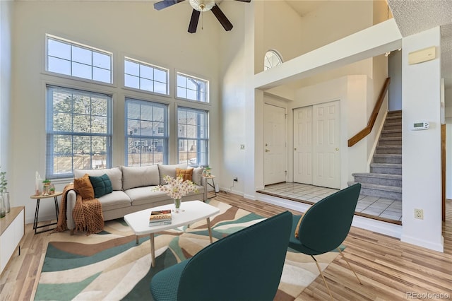 living area featuring baseboards, light wood finished floors, ceiling fan, stairs, and a towering ceiling