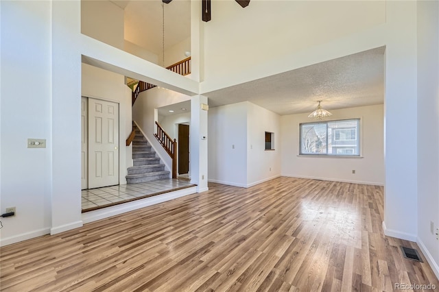 unfurnished living room with wood finished floors, visible vents, baseboards, stairs, and a textured ceiling