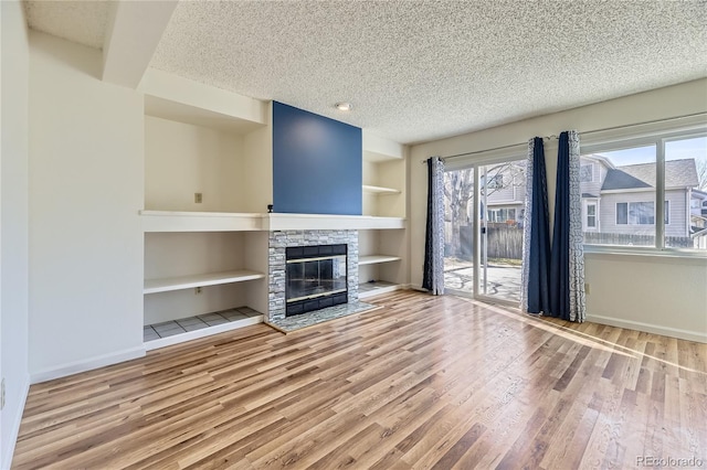 unfurnished living room featuring built in shelves, a textured ceiling, wood finished floors, a fireplace, and baseboards