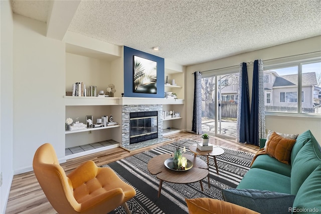 living area featuring a stone fireplace, light wood-style floors, baseboards, and a textured ceiling