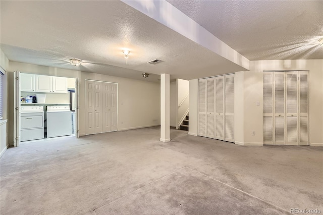 finished below grade area with visible vents, a textured ceiling, stairs, and washing machine and clothes dryer