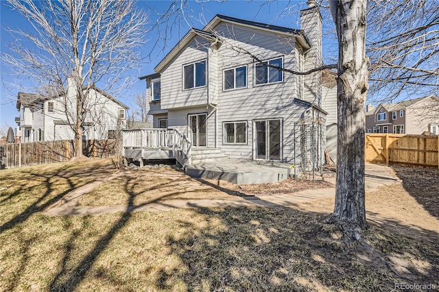 back of house featuring a wooden deck, a lawn, a chimney, a fenced backyard, and a patio area