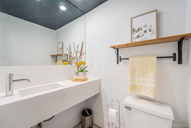 half bathroom with toilet, a sink, and recessed lighting