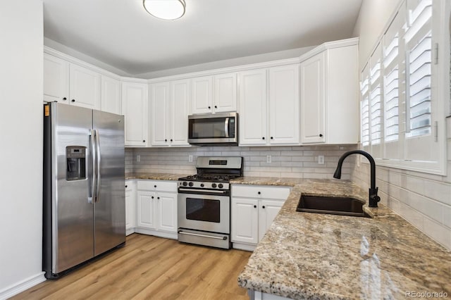 kitchen with a sink, stainless steel appliances, tasteful backsplash, and white cabinets