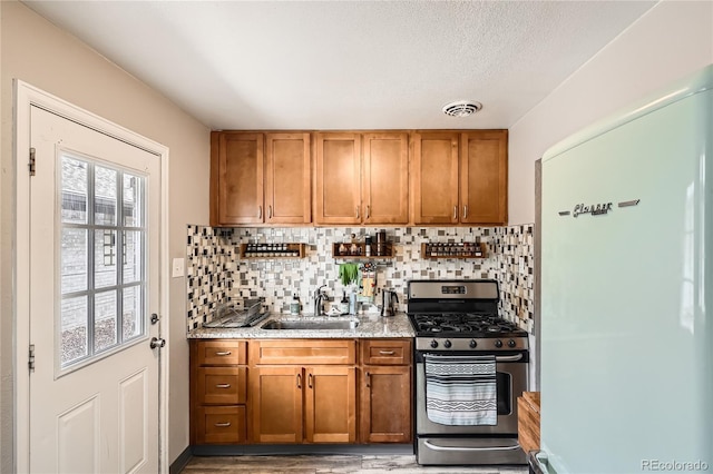 2955 N Gilpin St, Denver, CO 80205 - kitchen with freestanding refrigerator, stainless steel gas range, brown cabinets, and tasteful backsplash