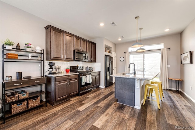 kitchen featuring light stone countertops, dark brown cabinets, an island with sink, and stainless steel appliances