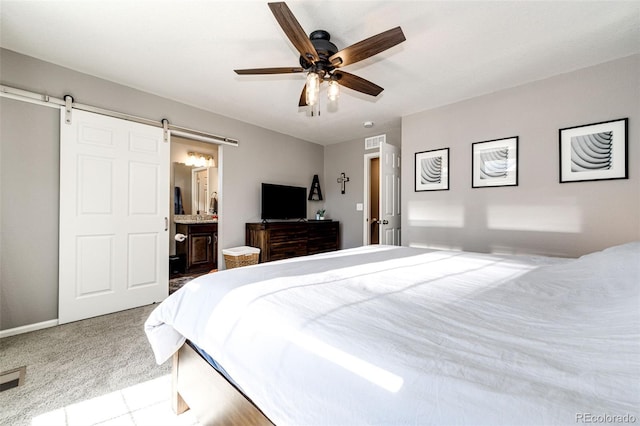 carpeted bedroom featuring a barn door, ceiling fan, and ensuite bath