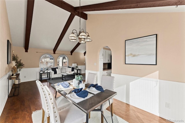 dining room with arched walkways, a wainscoted wall, wood finished floors, vaulted ceiling with beams, and a notable chandelier