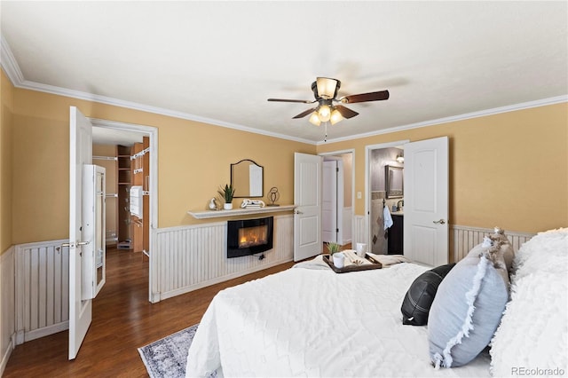 bedroom with a wainscoted wall, ornamental molding, dark wood-style flooring, and a glass covered fireplace