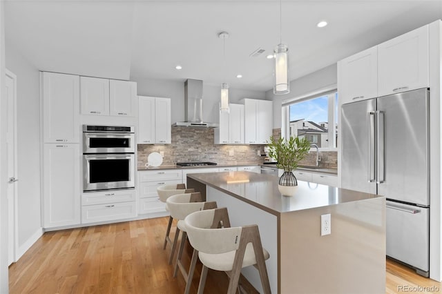 1284 Tennyson St Unit 1, Denver, CO 80204 - kitchen featuring stainless steel appliances, wall chimney exhaust hood, a center island, backsplash, and white cabinets